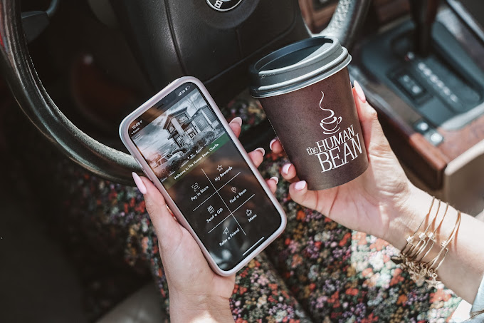 A cell phone in one hand and a Human Beans Coffee in the other hand