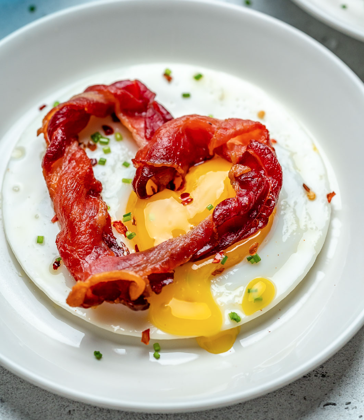 Sunny-side up egg with a heart shaped bacon on top.