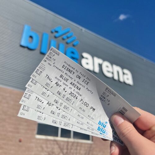 Disney on Ice tickets are held in front of the Blue FCU Arena sign.