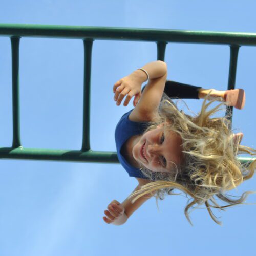 A girl hangs upside down from playground equipment.