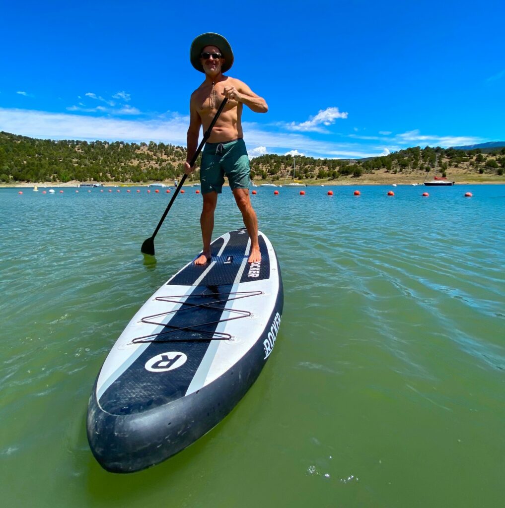 A man stands on top of an inflatable paddle board on a sunny day in Carter Lake.