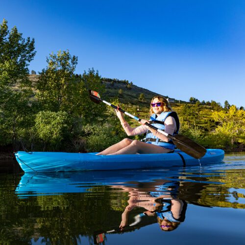 A woman in a kayak rows across carter lake on a summer day.