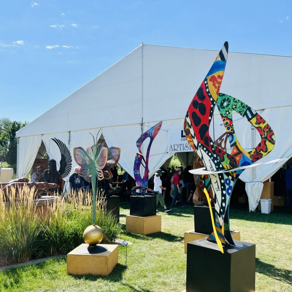 Sculptures sit outside of a tent at Sculpture in the Park at Benson Sculpture Garden.