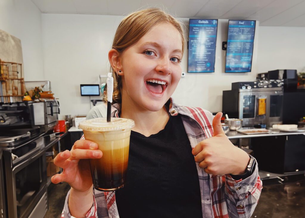 A barista at Colorado Coffee holds a drink while giving a thumbs up.