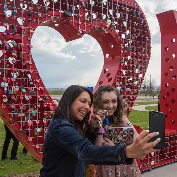 Two women posing for a selfie in front of Loveland's Love Lock sculpture