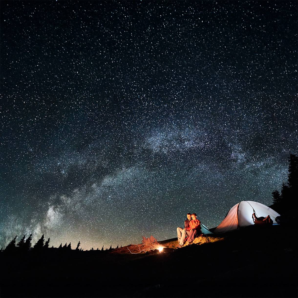 Campers look upon a night sky full of stars.
