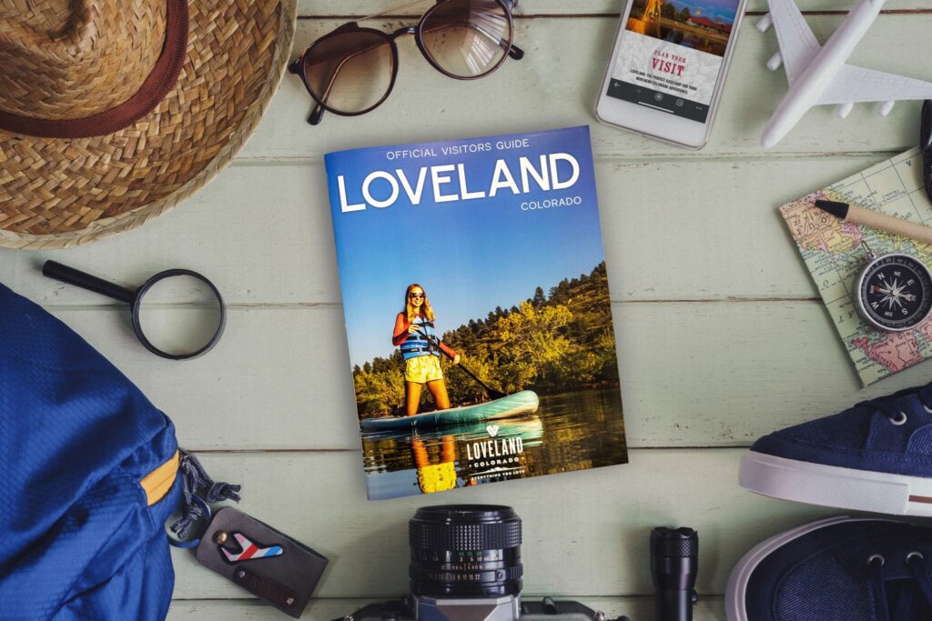 A copy of the Official Loveland Visiotrs Guide over a beige background with other travel related items at the edge of the photo.